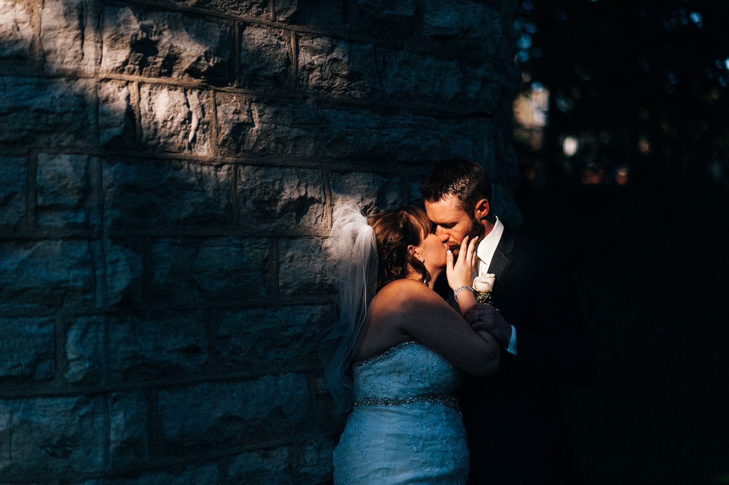 Dramatic nighttime portrait against textured stone wall with creative lighting.