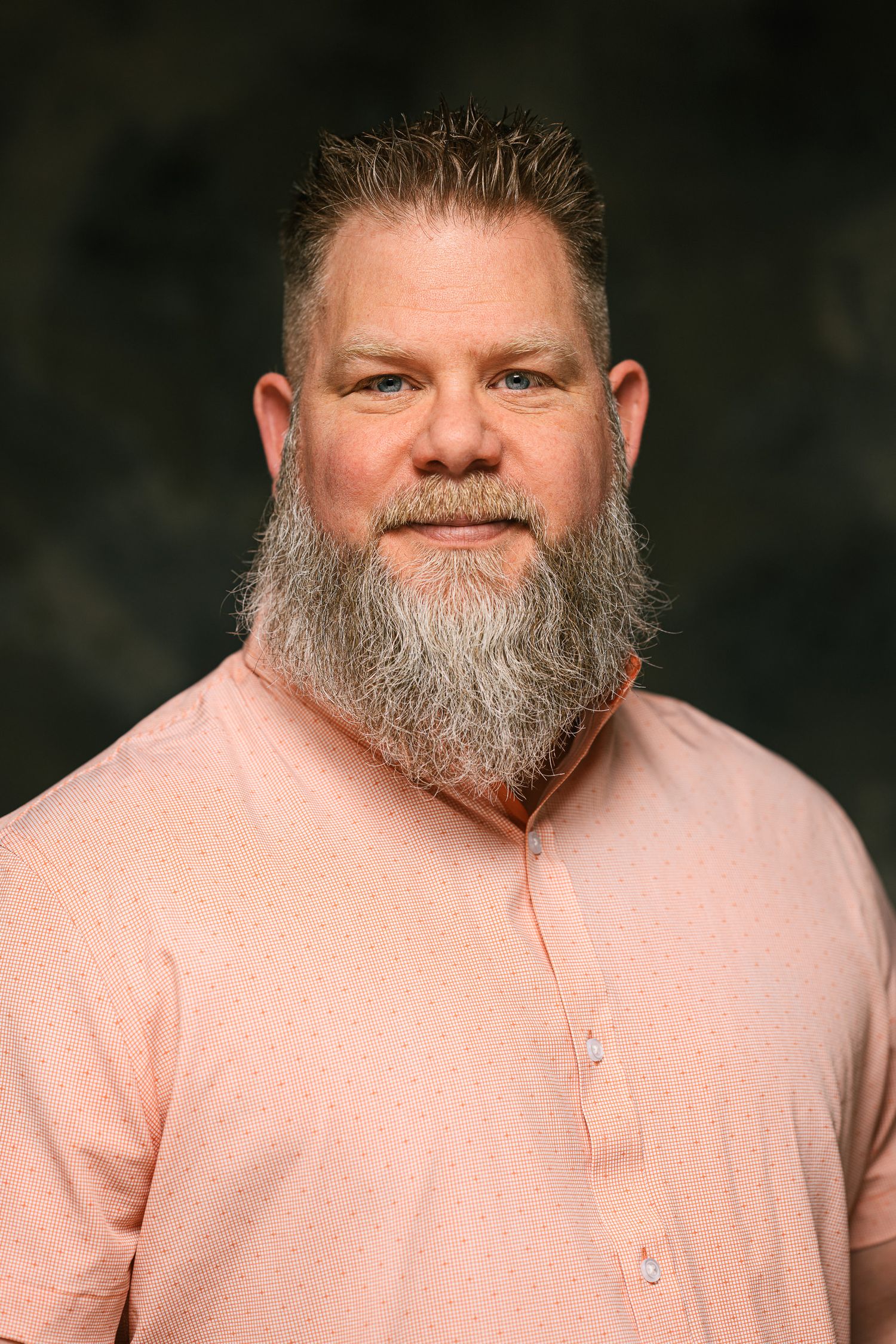 Person wearing a pink henley shirt smiles warmly at the camera against a dark background.