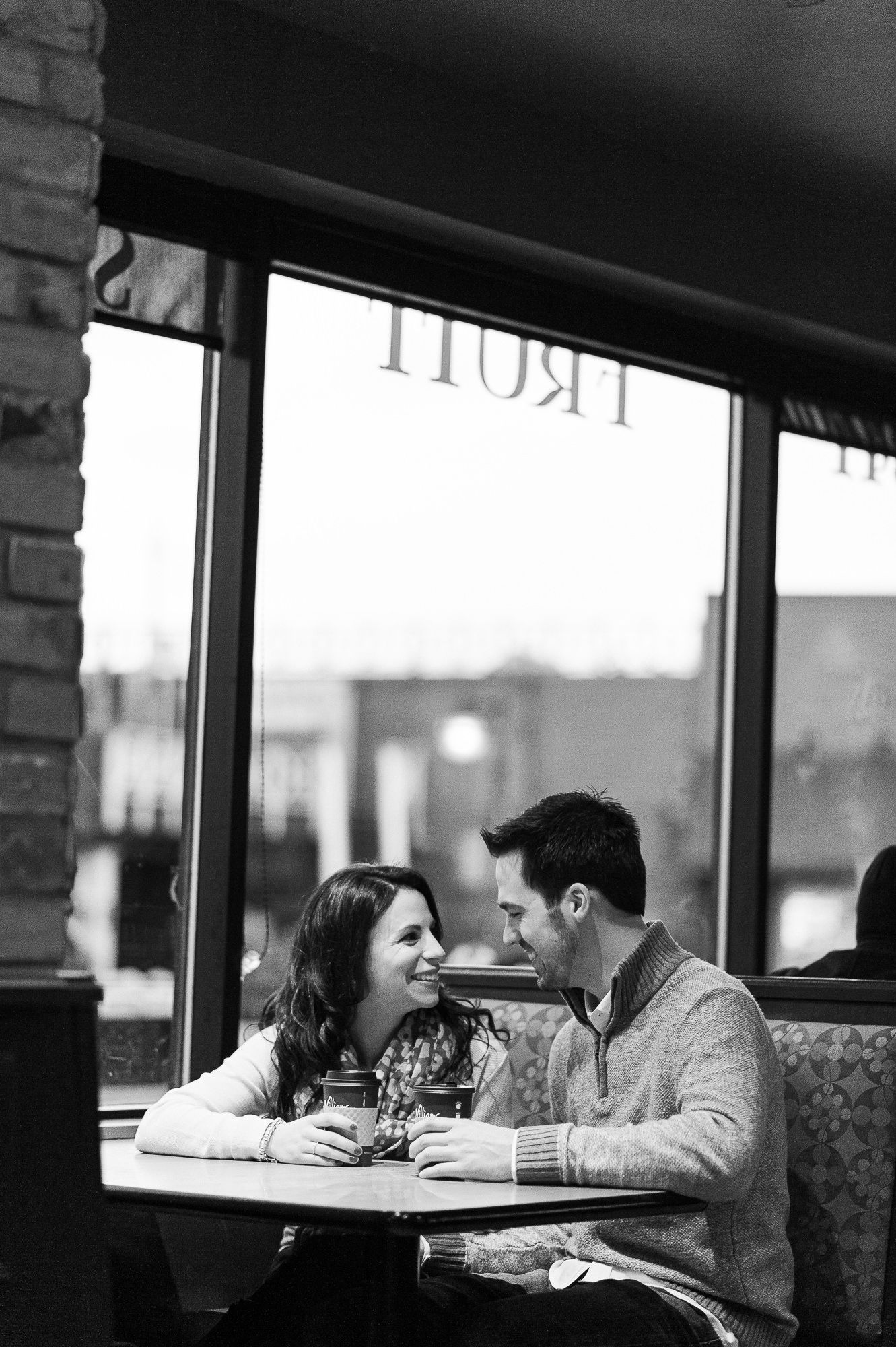 Couple sharing intimate moment at cafe table by window.