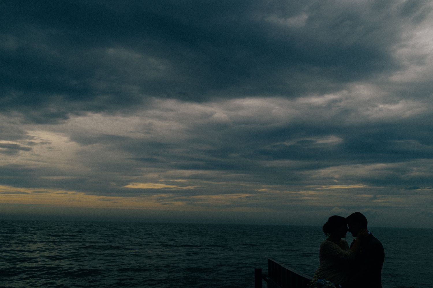 Silhouetted couple against moody sunset sky over ocean horizon.