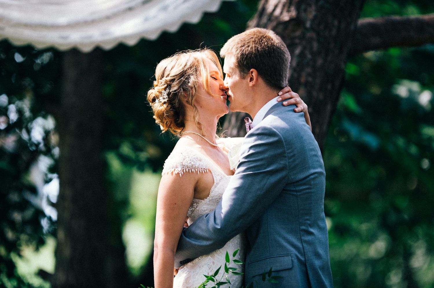 Newlywed couple sharing intimate moment under green foliage.