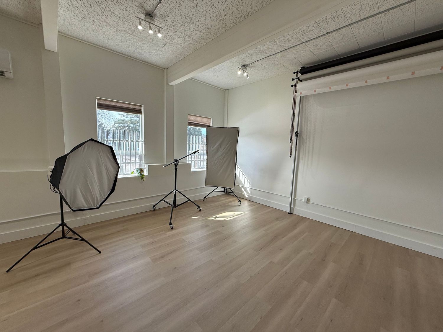 A bright, empty photography studio space with hardwood floors, white walls, and professional lighting equipment.