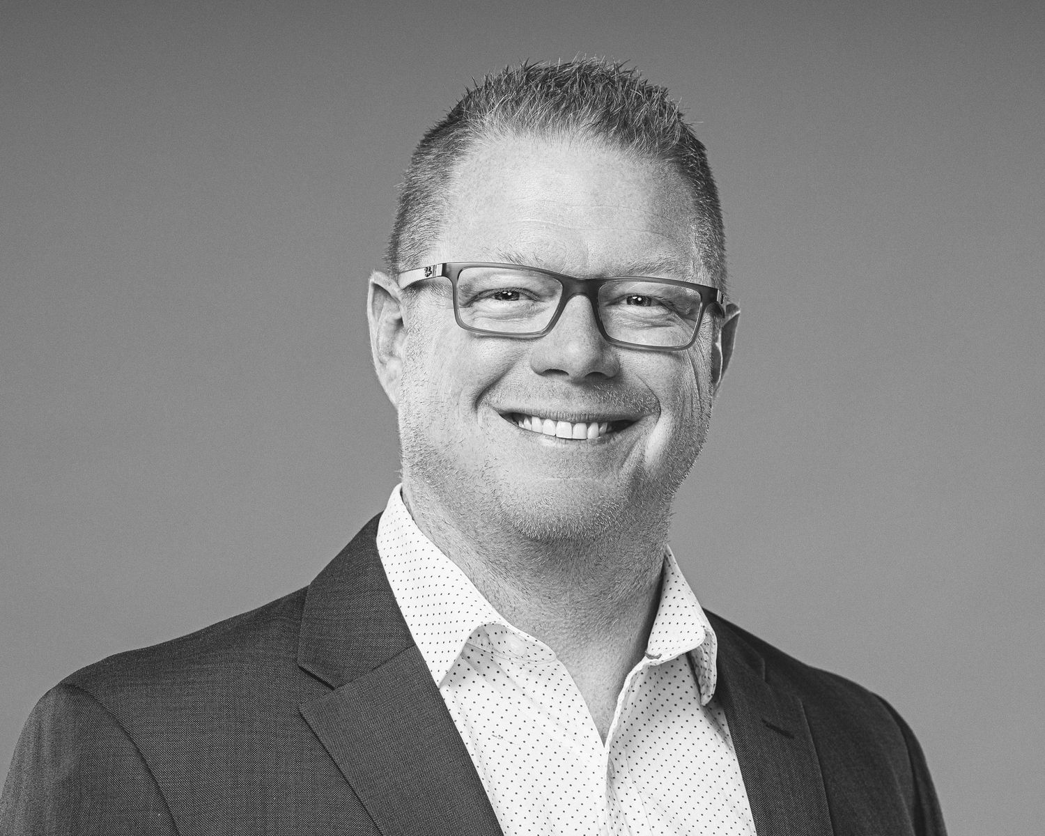 Professional black and white headshot of someone in glasses and business attire smiling warmly at the camera.
