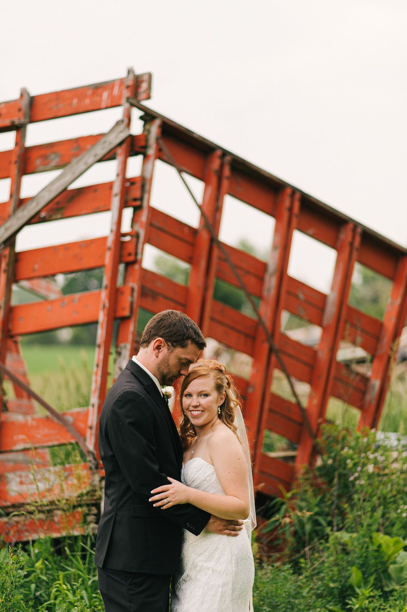 Romantic couple portrait by rustic red wooden fence structure.