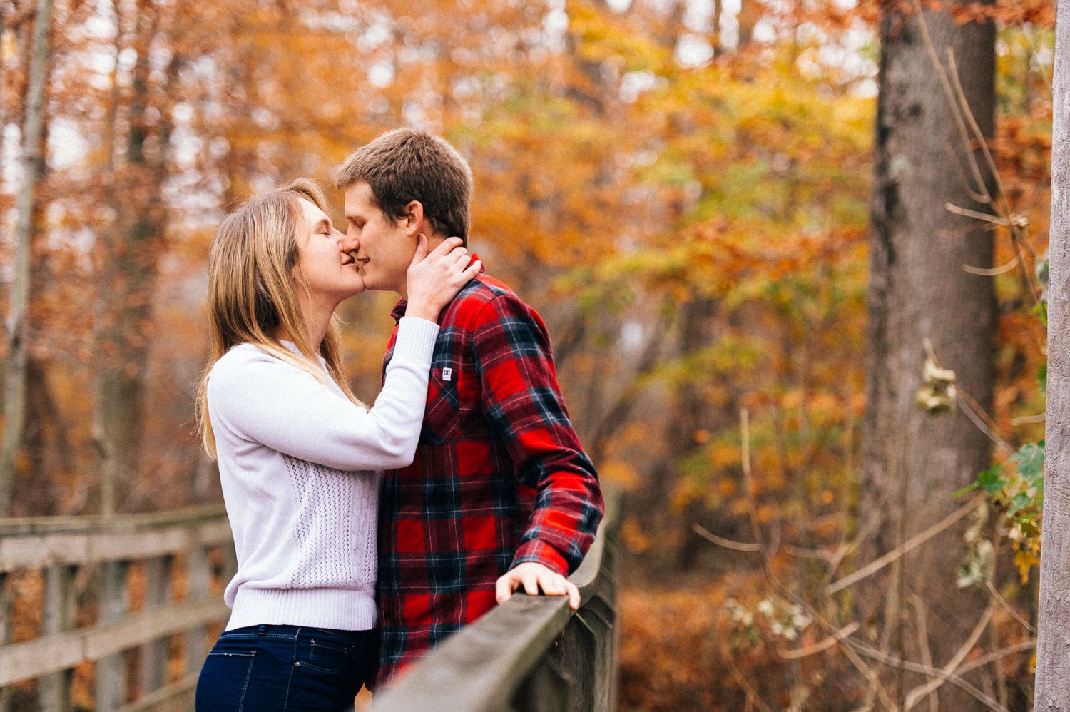 Couple embracing in a forest surrounded by orange fall leaves.