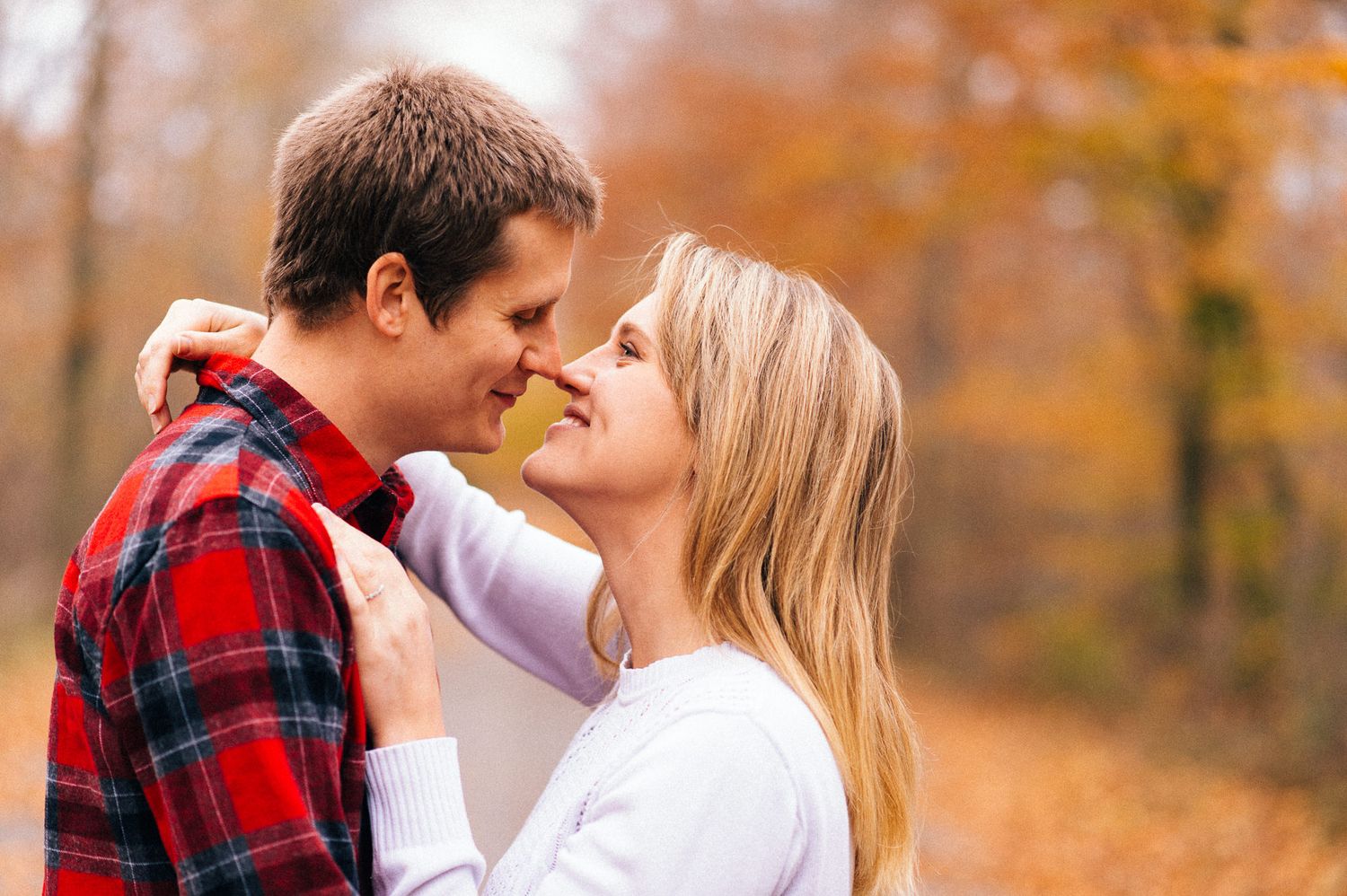 Romantic autumn engagement photo in a forest with fall foliage.