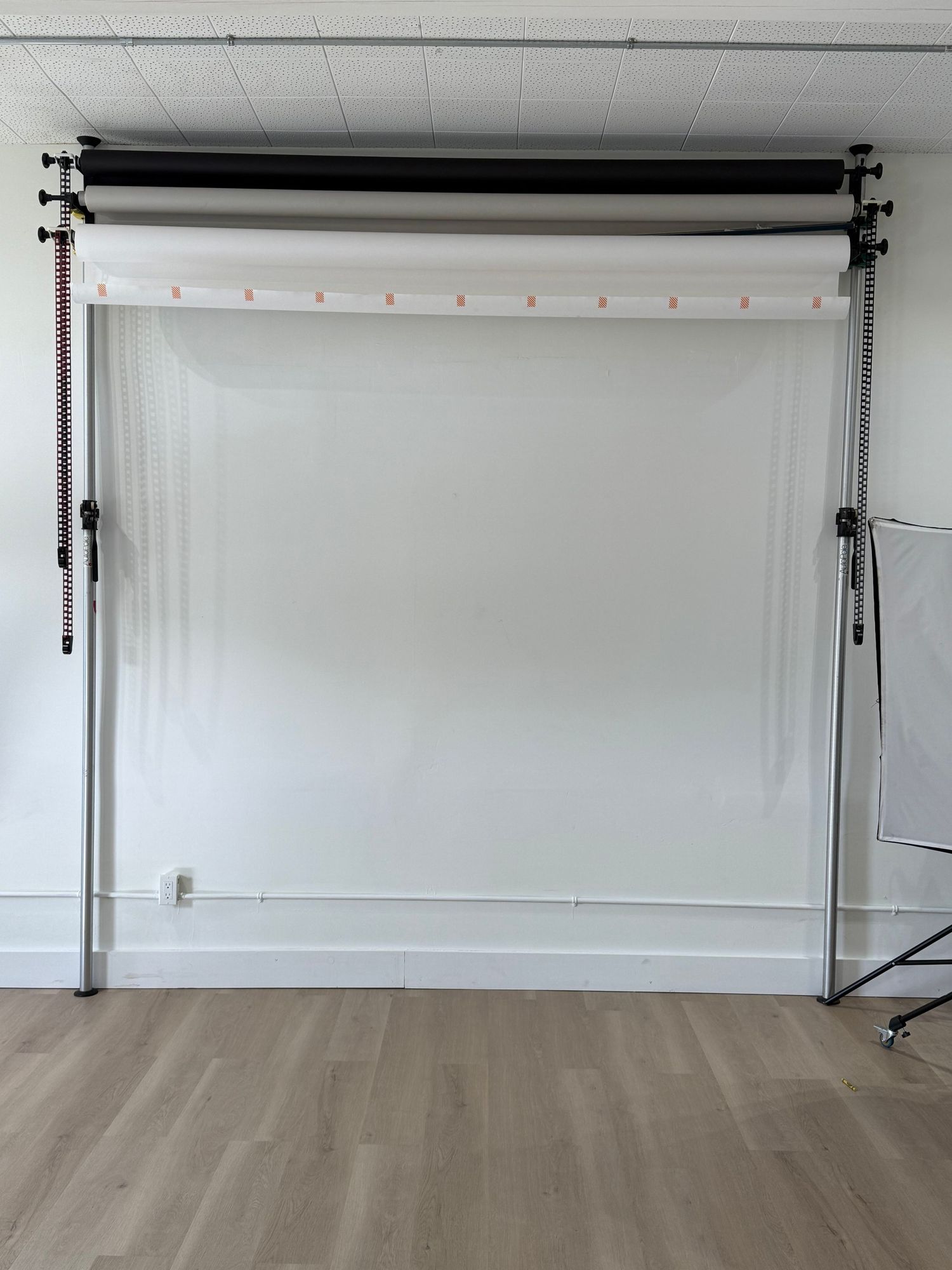 A white backdrop photography studio setup with black mounting bars and lighting equipment against a clean wall.