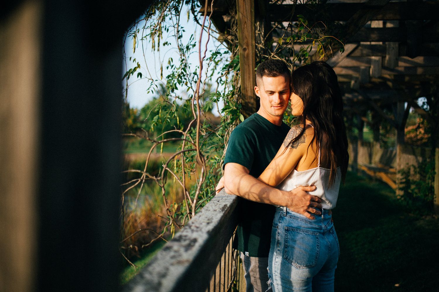 A couple shares an intimate embrace on a wooden bridge surrounded by greenery.