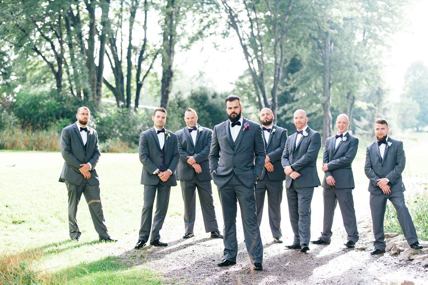 Groomsmen in dark suits posed together on a rustic path.