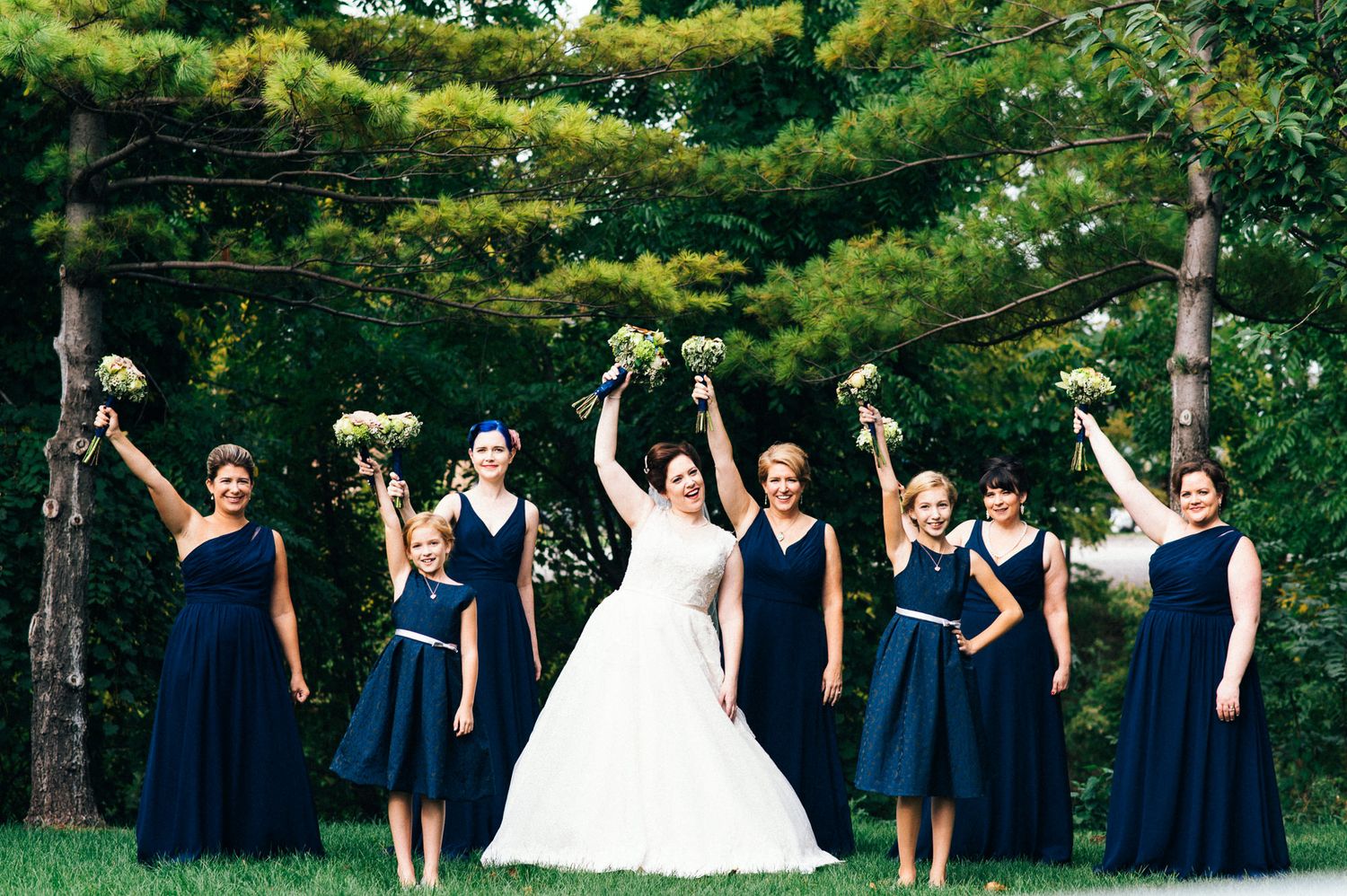 Wedding party in navy blue dresses and suits posing outdoors in a garden setting.