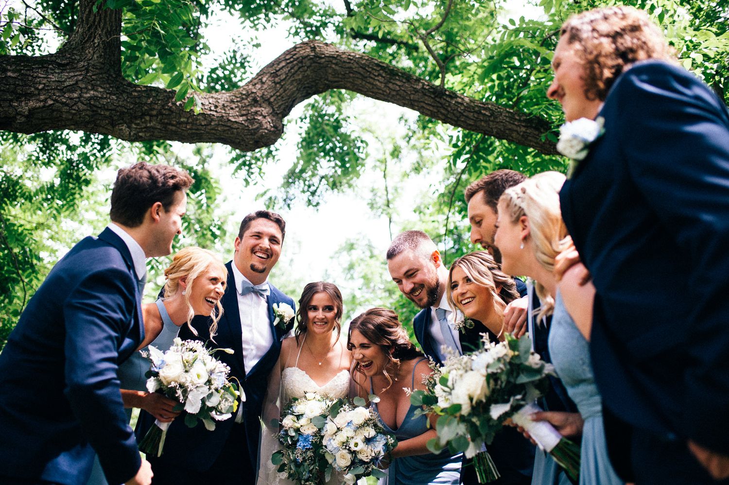 Wedding party celebrating outdoors under lush green trees.