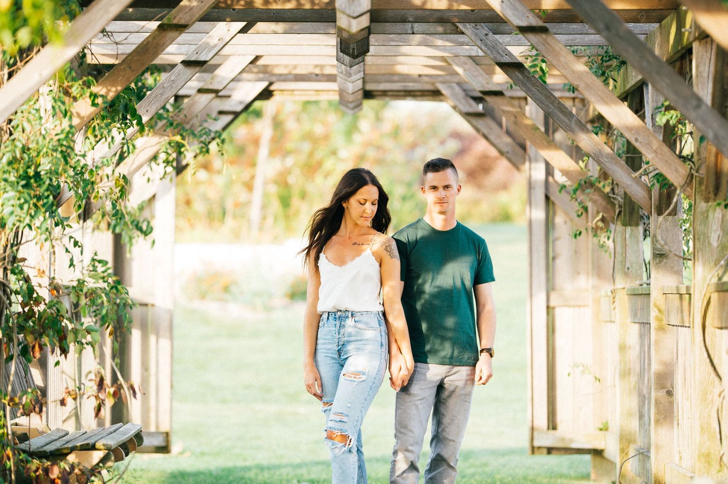 Couple walks together under a rustic wooden pergola surrounded by greenery.