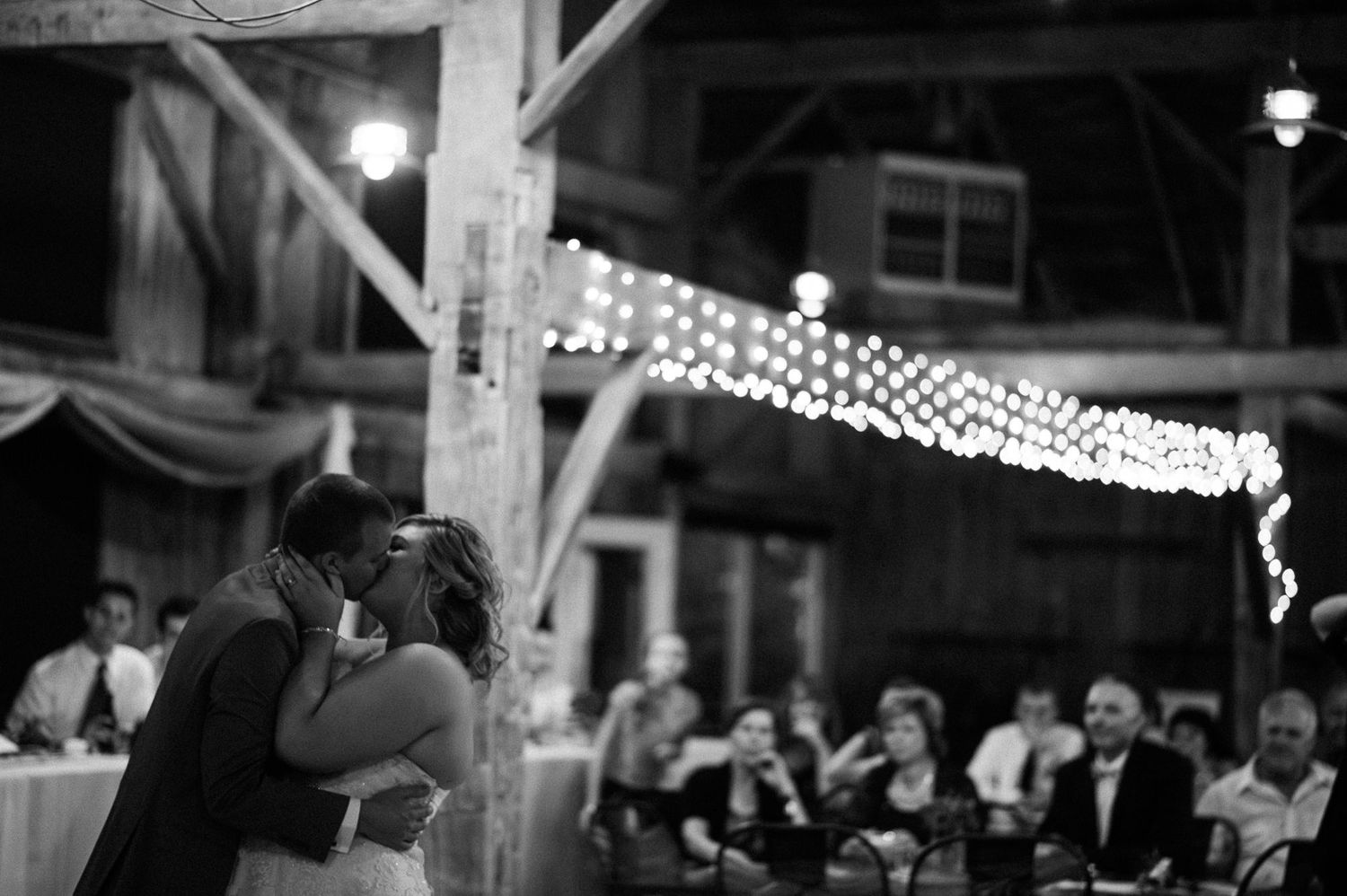 Wedding reception venue decorated with romantic string lights and rustic wooden beams.