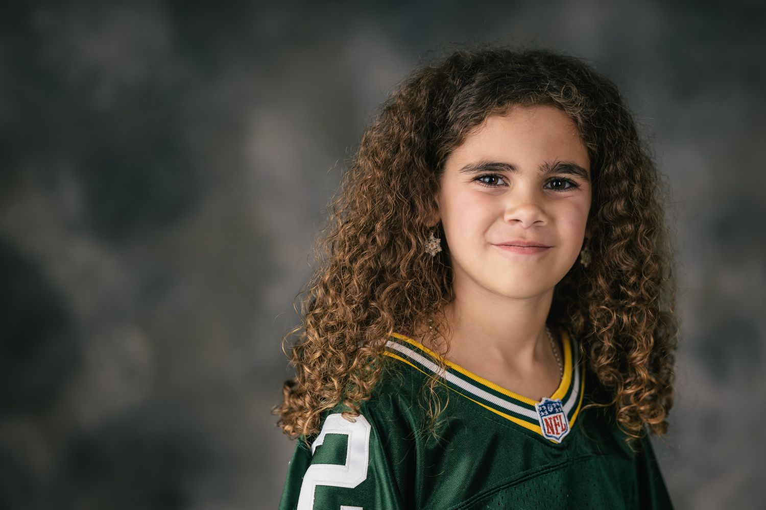Child wearing green sports jersey poses for multiple portrait shots against dark backdrop.