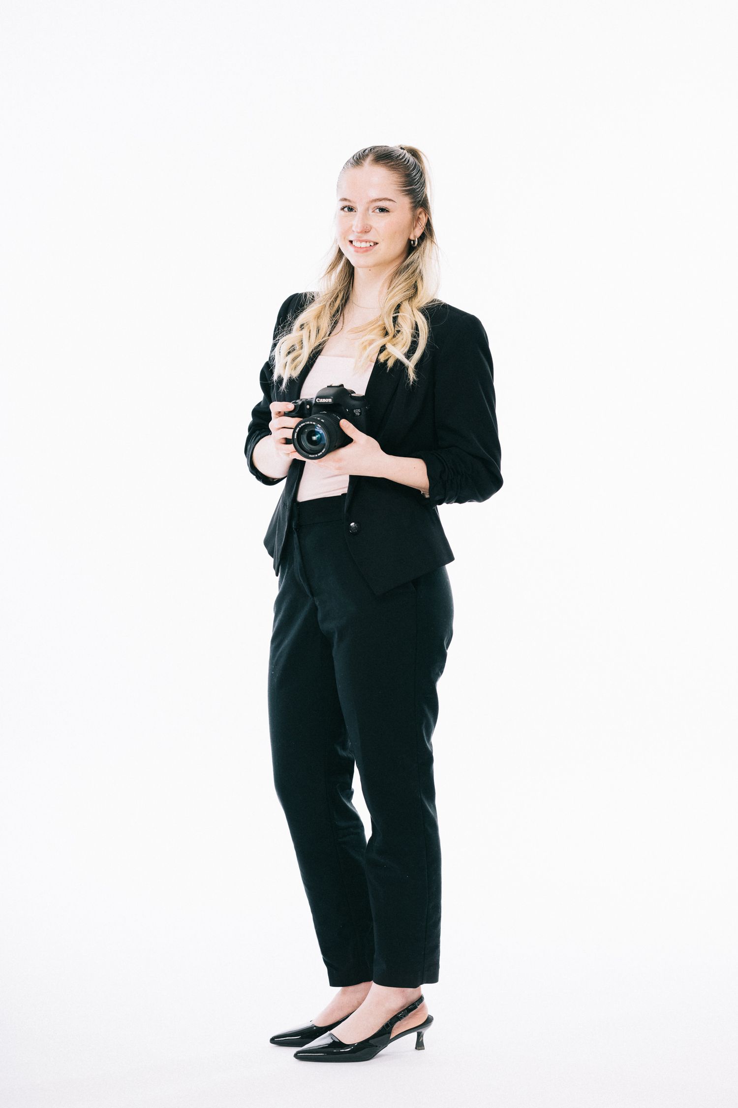 Woman in black business attire posing with camera in studio portraits.