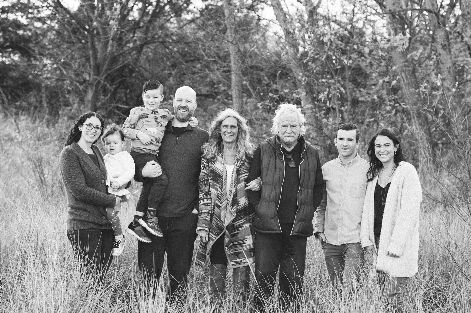 Extended family group poses together outdoors in casual attire against a natural background.