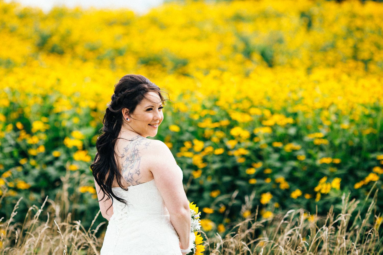Bride posing in field of bright yellow wildflowers on sunny day.
