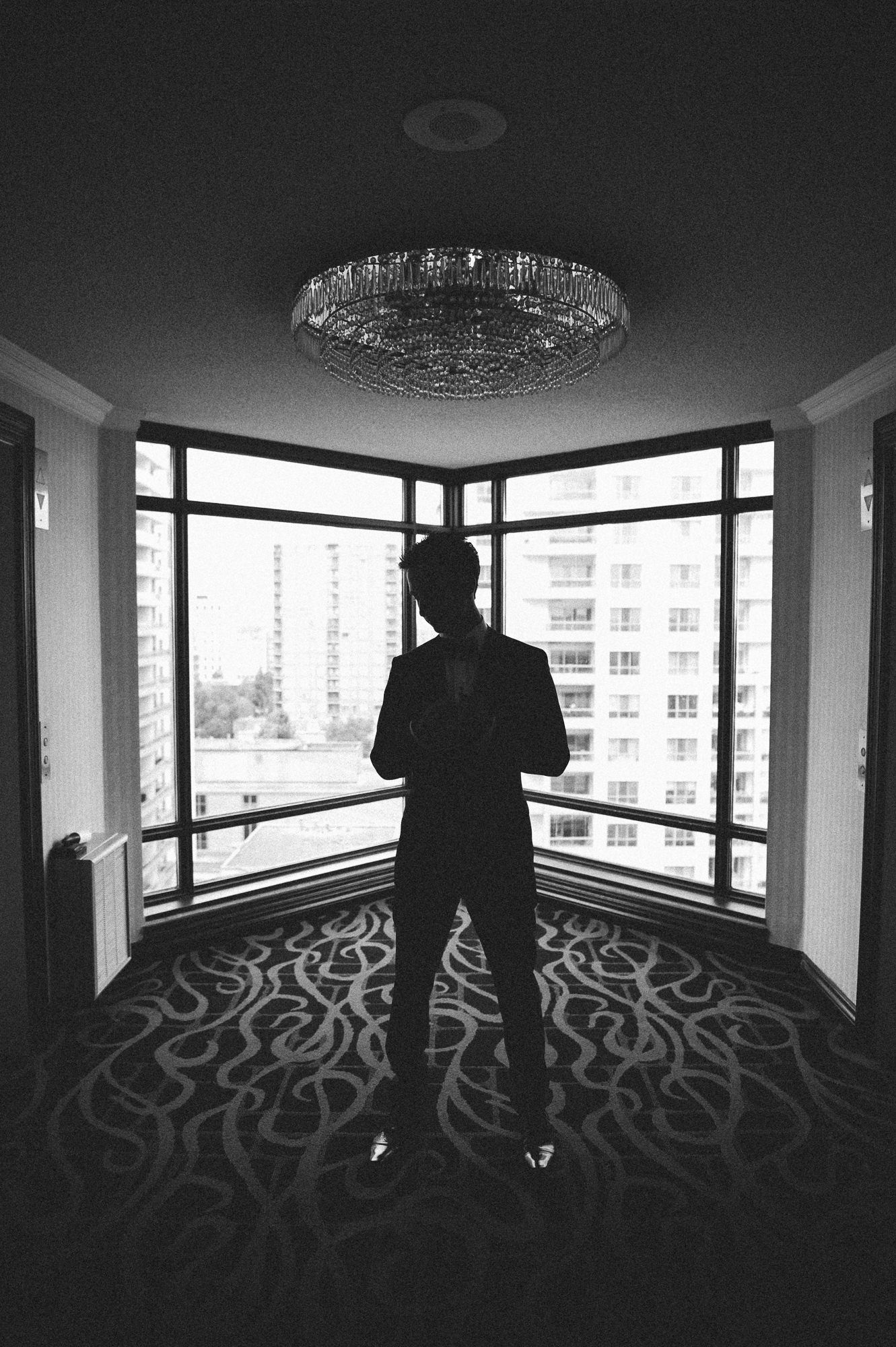 Silhouette of person standing in modern room with elegant chandelier and city views.