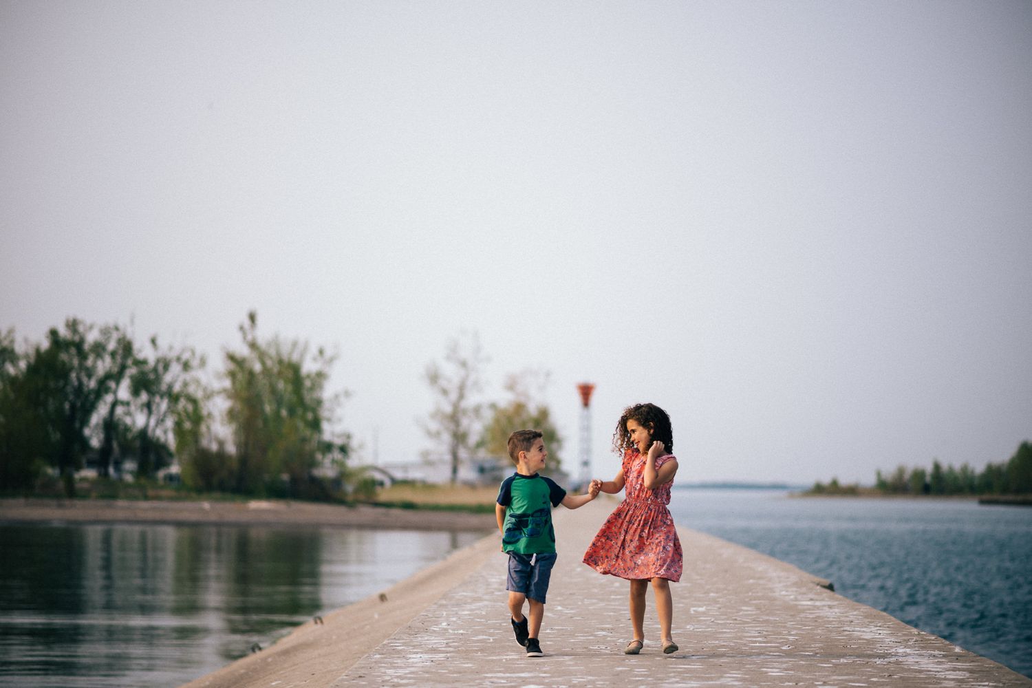 People walking along a waterfront path with lighthouse visible in the distance.