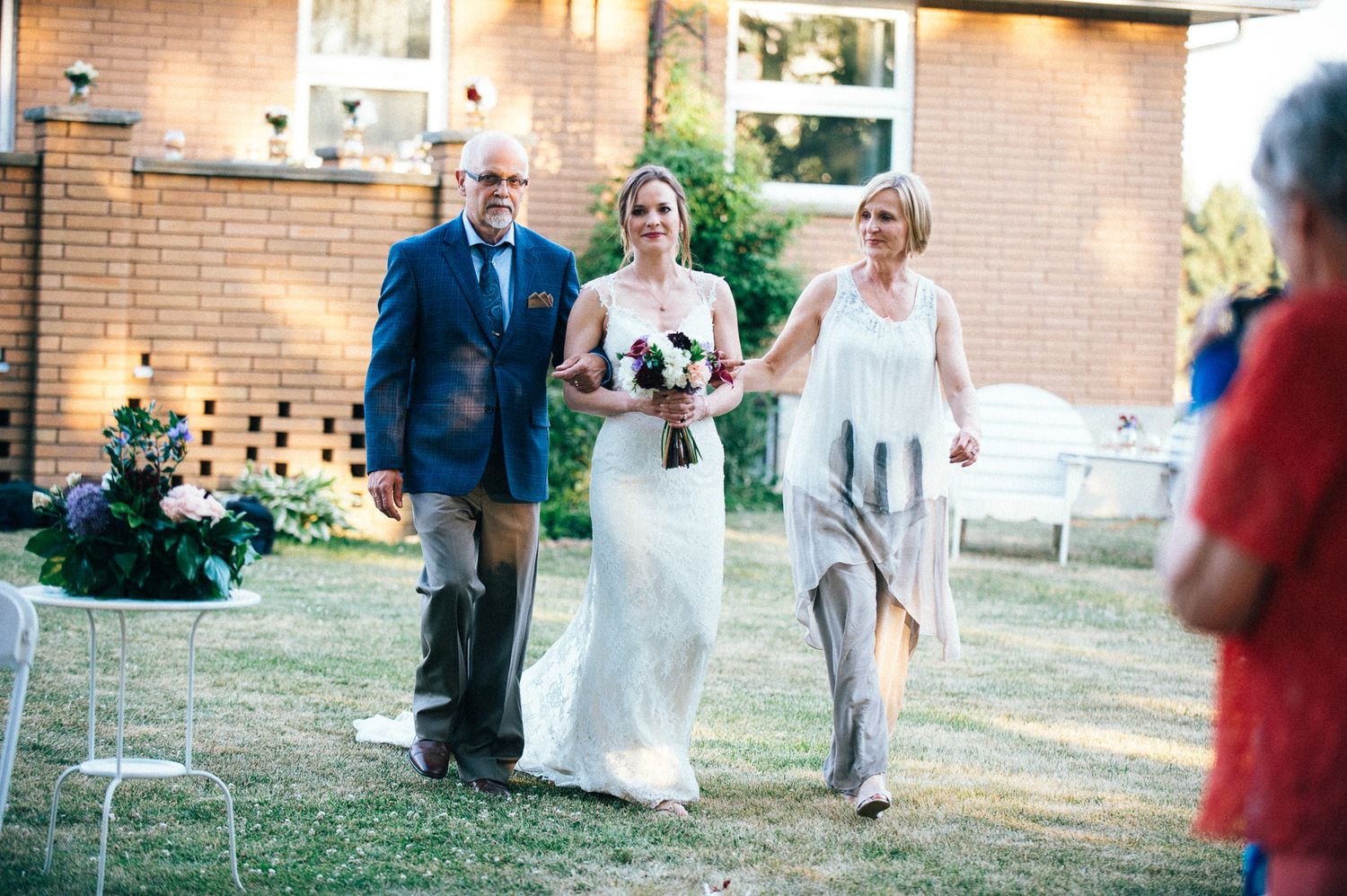 A wedding party poses and celebrates outdoors near a brick building on a sunny day.