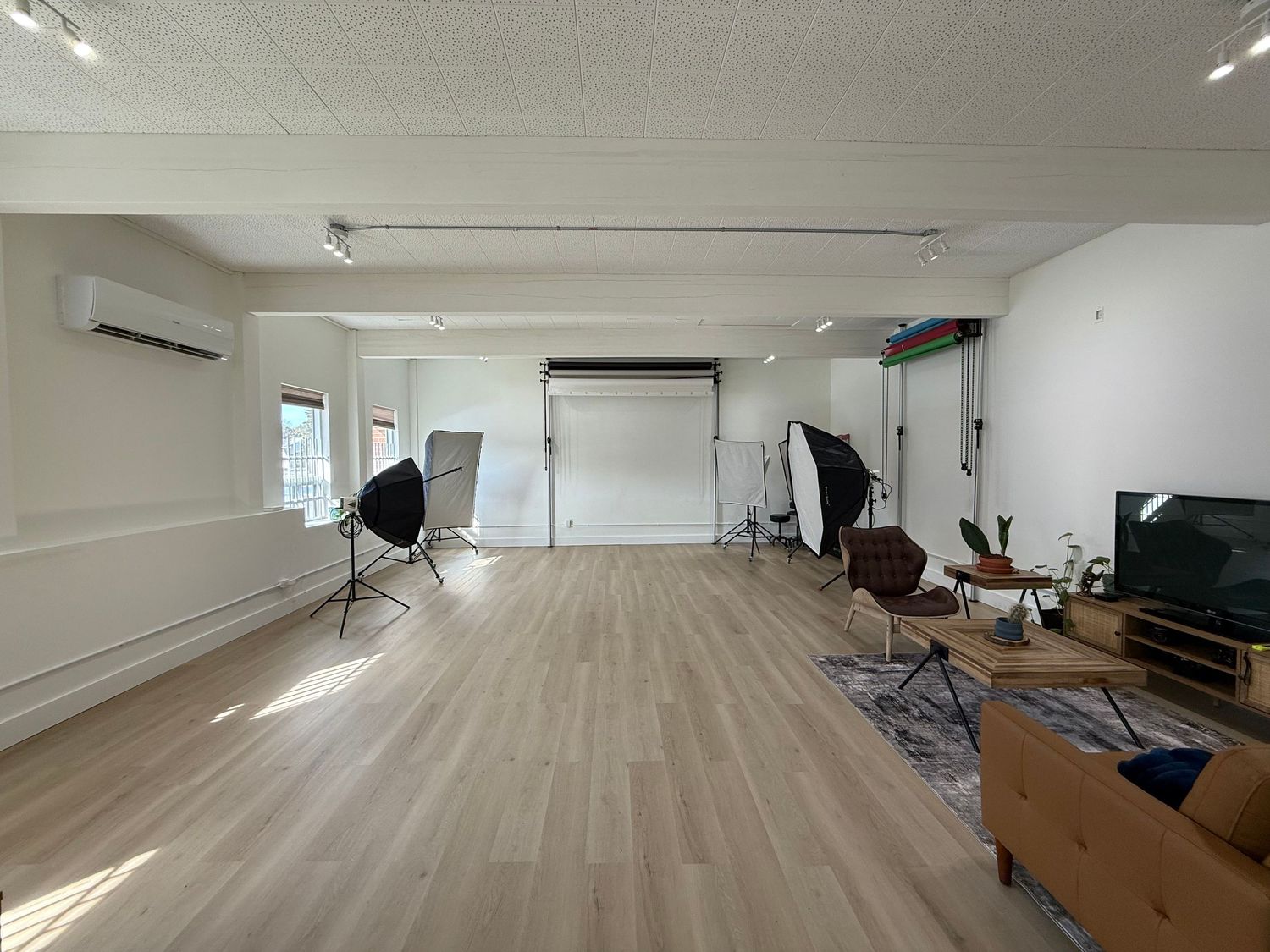 Empty photography studio with wooden floors, white walls, and professional lighting equipment.
