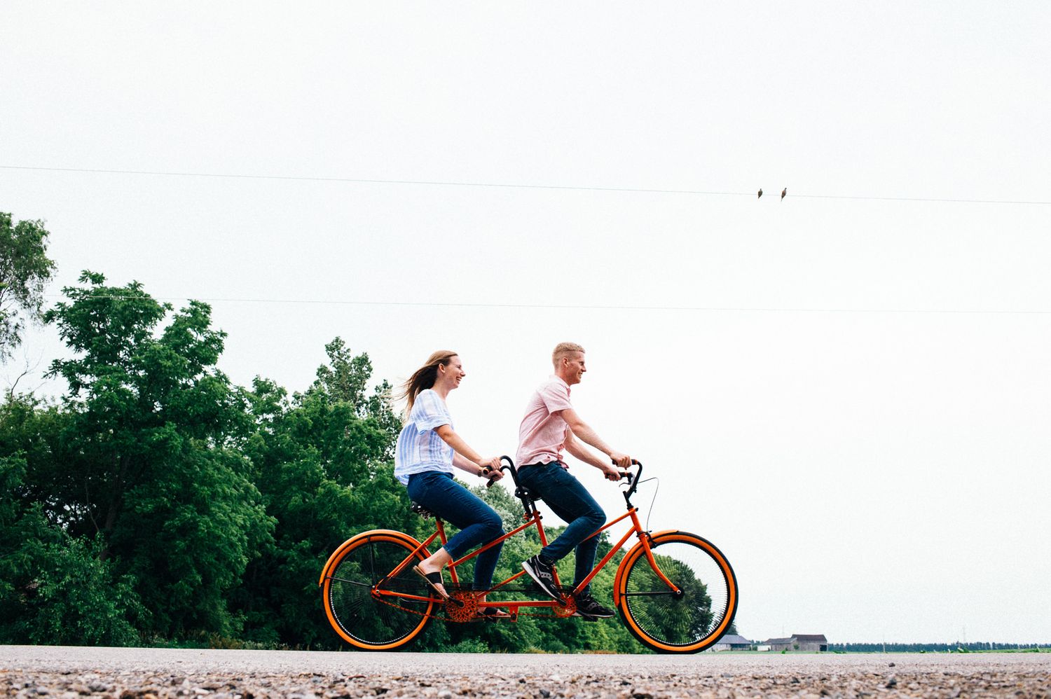 Playful couple enjoying a ride on an orange tandem bicycle against white sky.