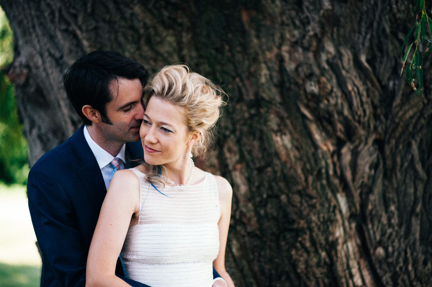 Romantic wedding couple embracing near trees in an outdoor setting.