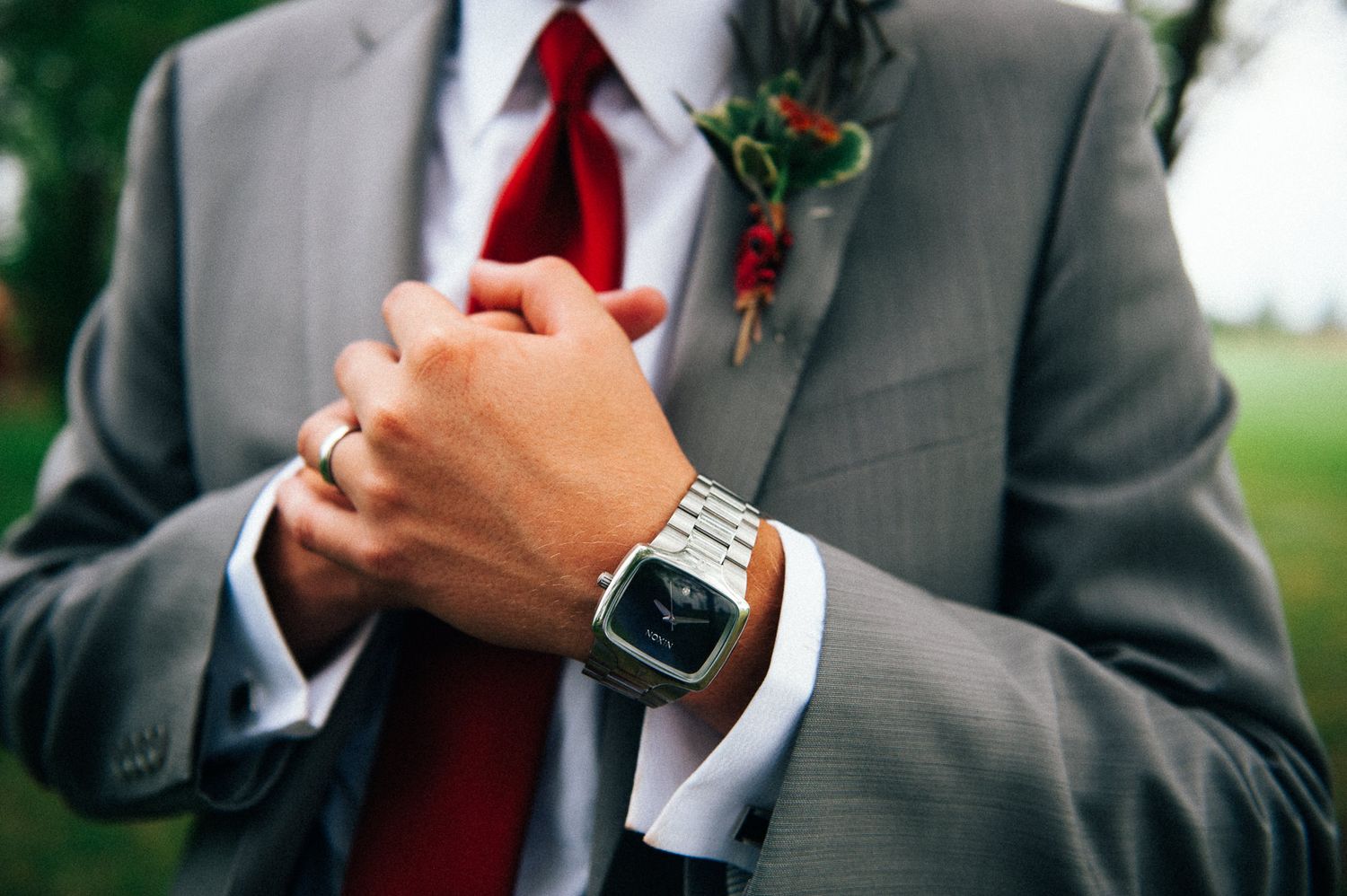 Detail shot of groom's hands showing watch and boutonniere against grey suit.