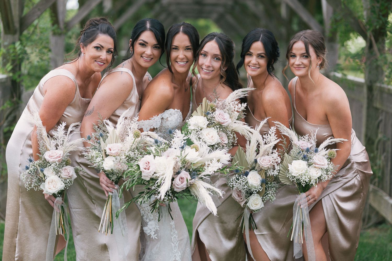 Bridal party in neutral tones holding elegant white and green bouquets.