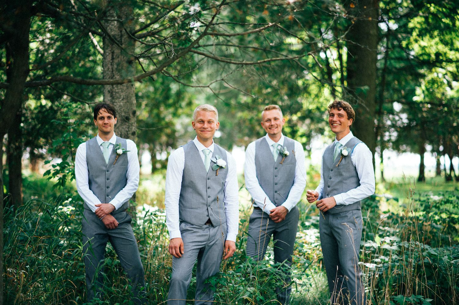 Groomsmen in gray vests and suits standing together in a lush garden setting.