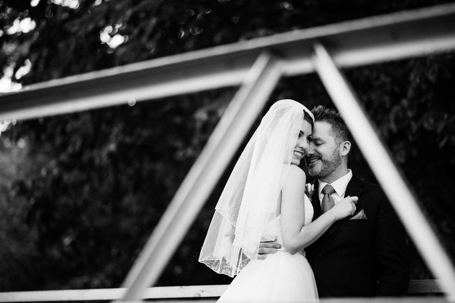 Artistic black and white wedding portrait showing couple embracing under geometric architecture.
