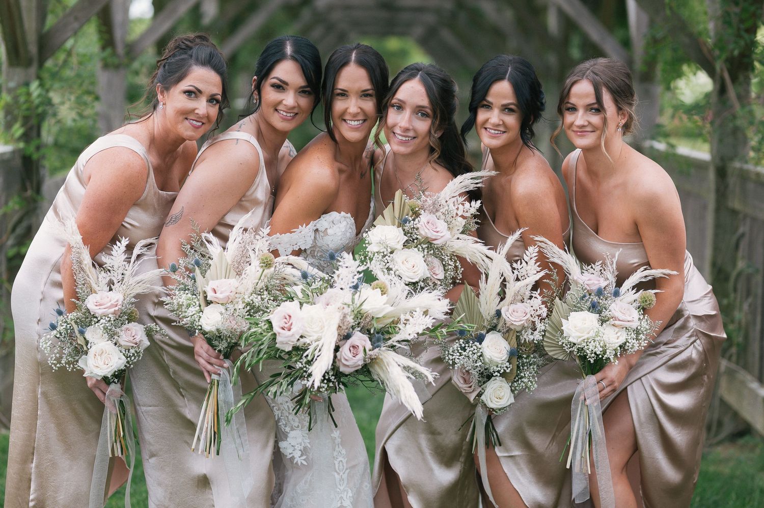 Bridesmaids in elegant gray dresses hold white floral bouquets while posing together outdoors.