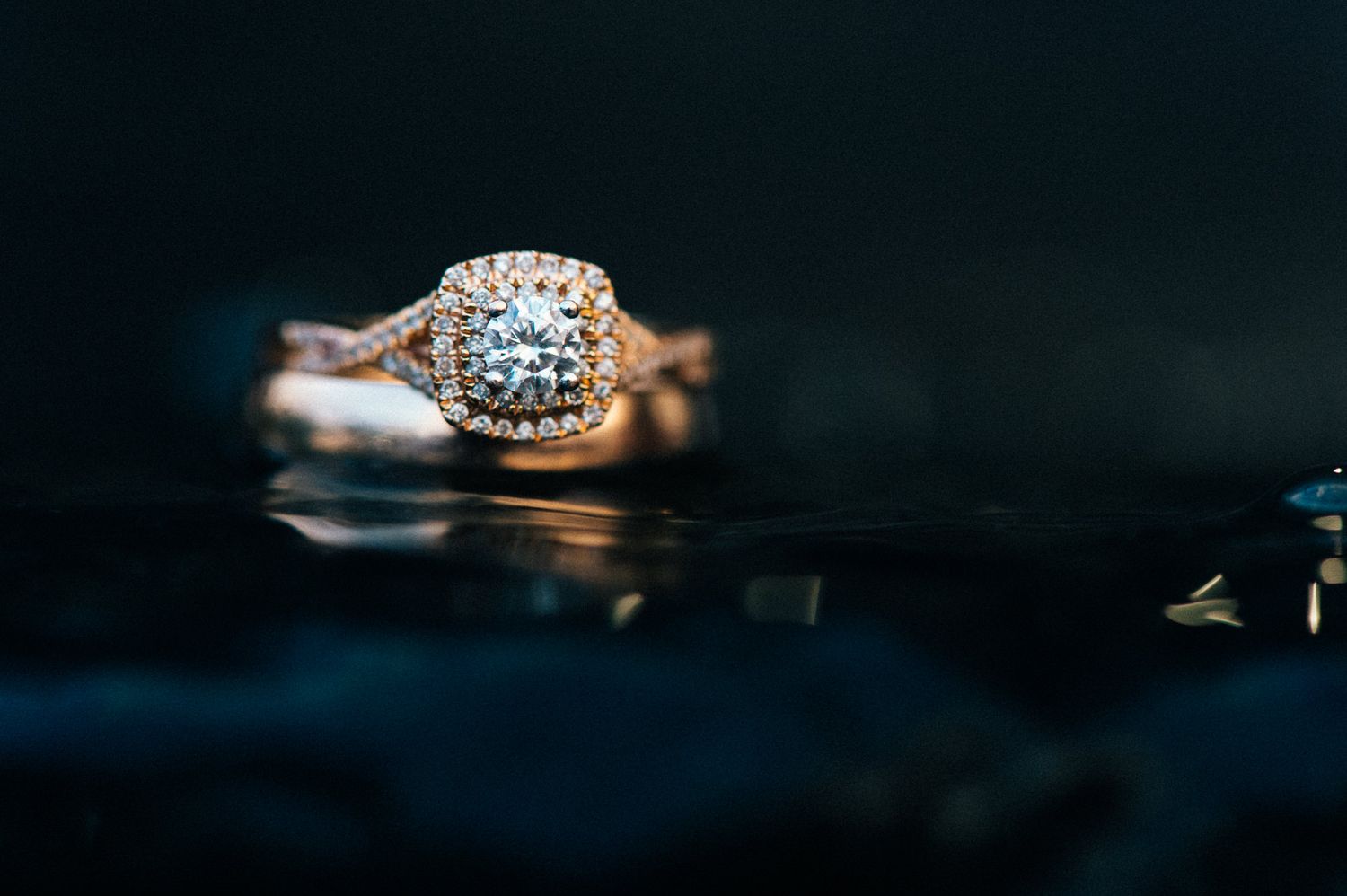 Close-up of an elegant diamond engagement ring with halo setting against dark background.