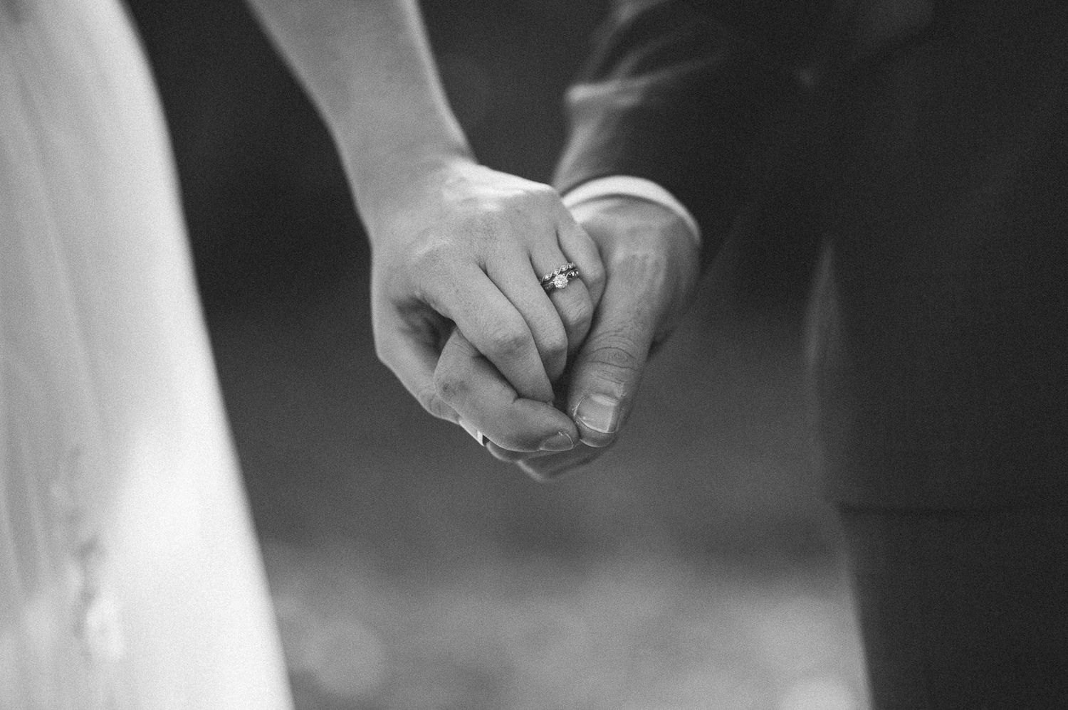 Black and white close-up of hands holding during wedding ceremony.