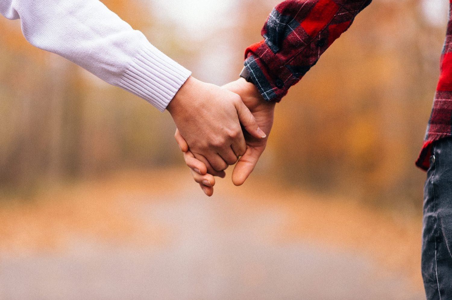 Close-up of hands reaching toward each other against autumn background.