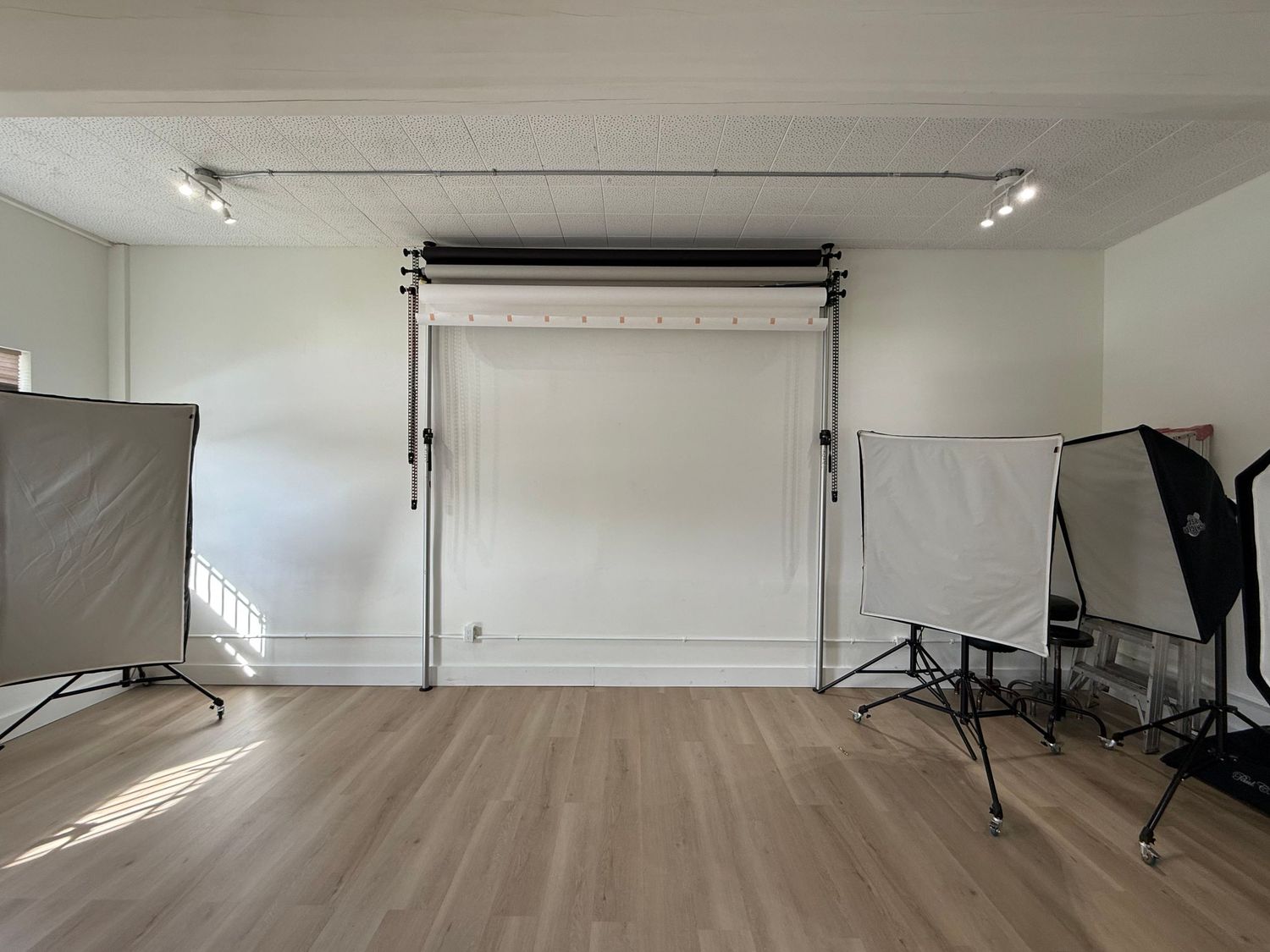 Empty white photography studio with lighting equipment and seamless backdrop setup for professional photoshoots.