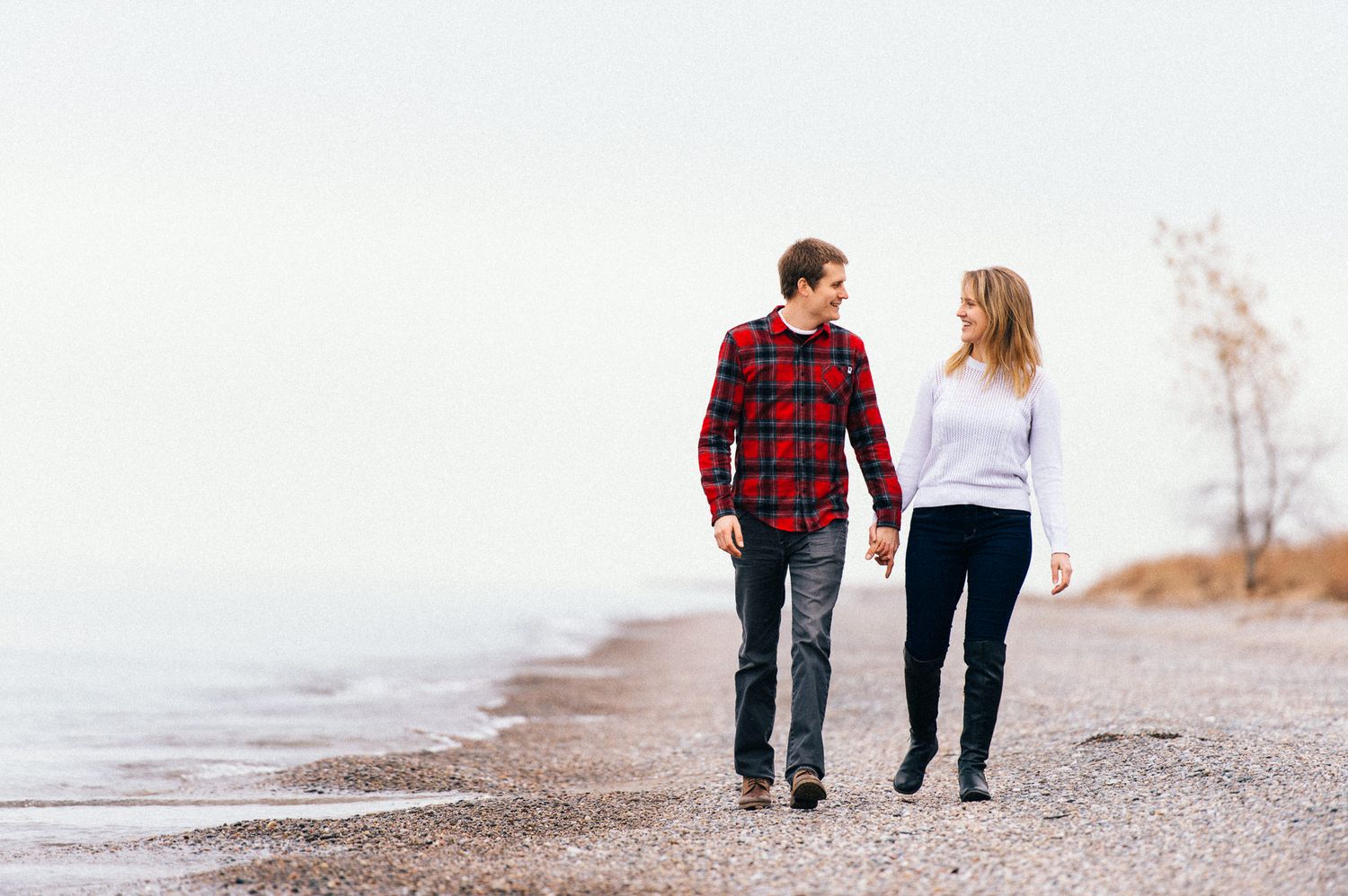 Couple strolling along a misty beach shoreline in casual attire.