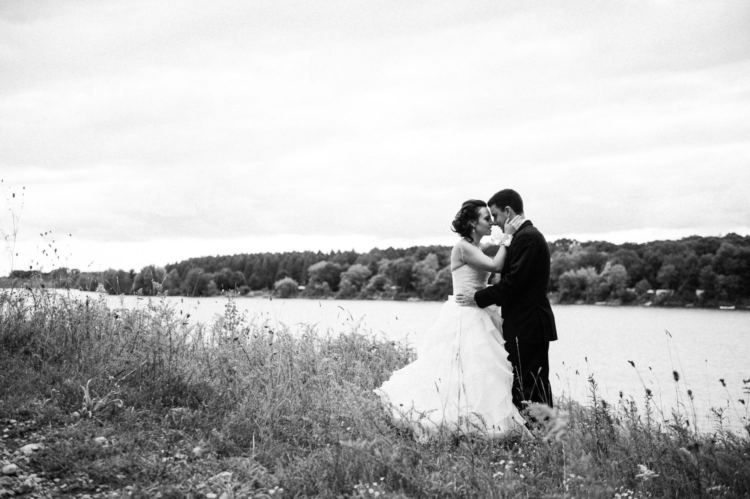 Black and white portrait of couple embracing by lakeside on their wedding day.