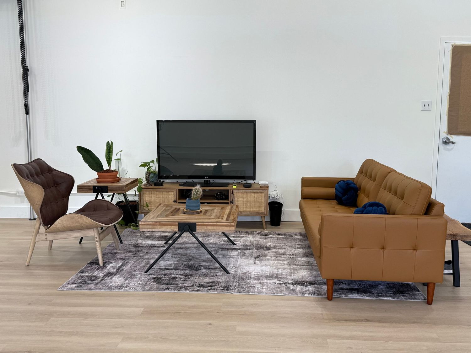 Modern living room with tan leather sofa, brown accent chair, wooden TV stand and geometric coffee table on gray area rug.
