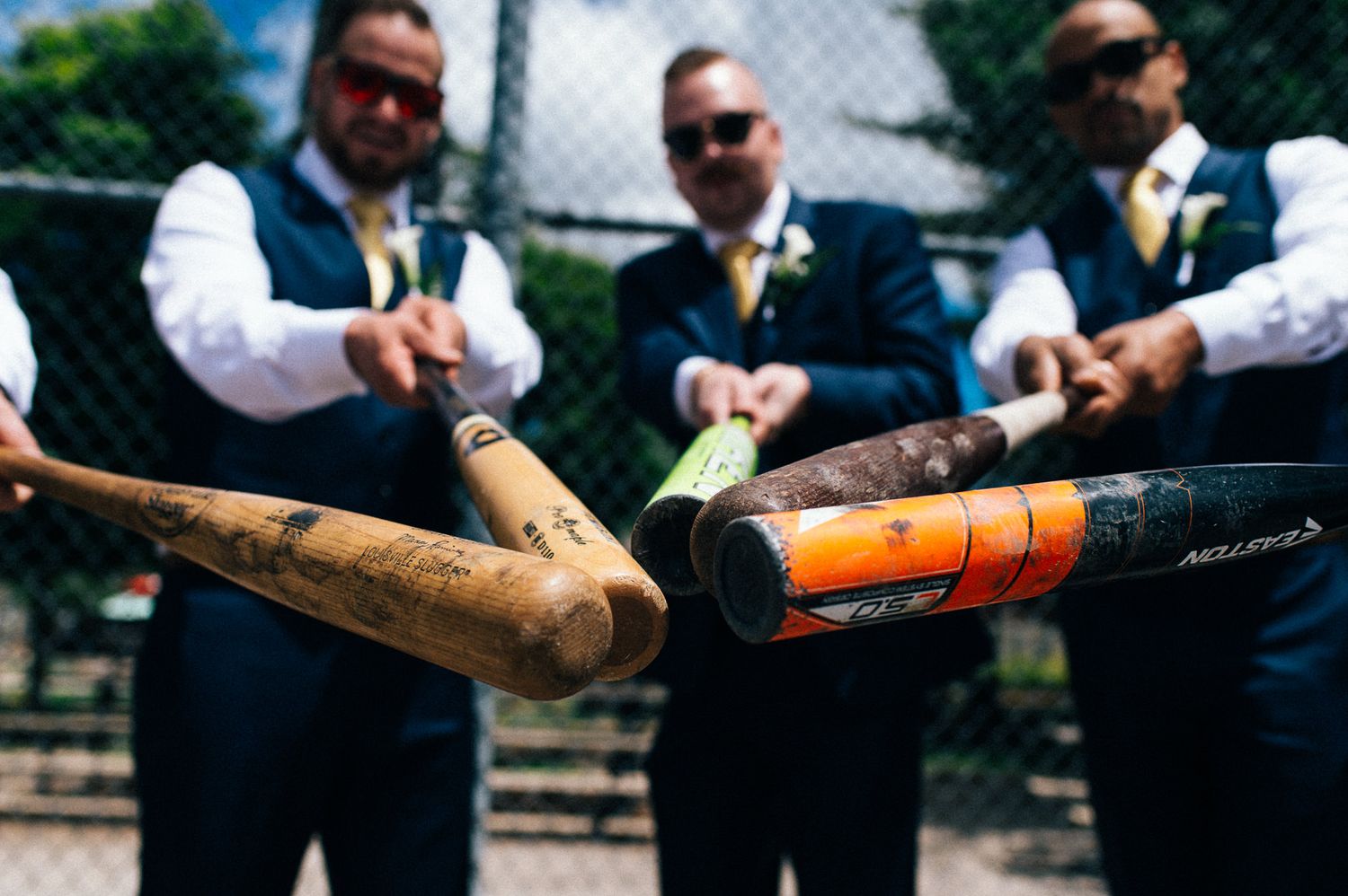 Groomsmen hold baseball bats together in a unique wedding photo pose.