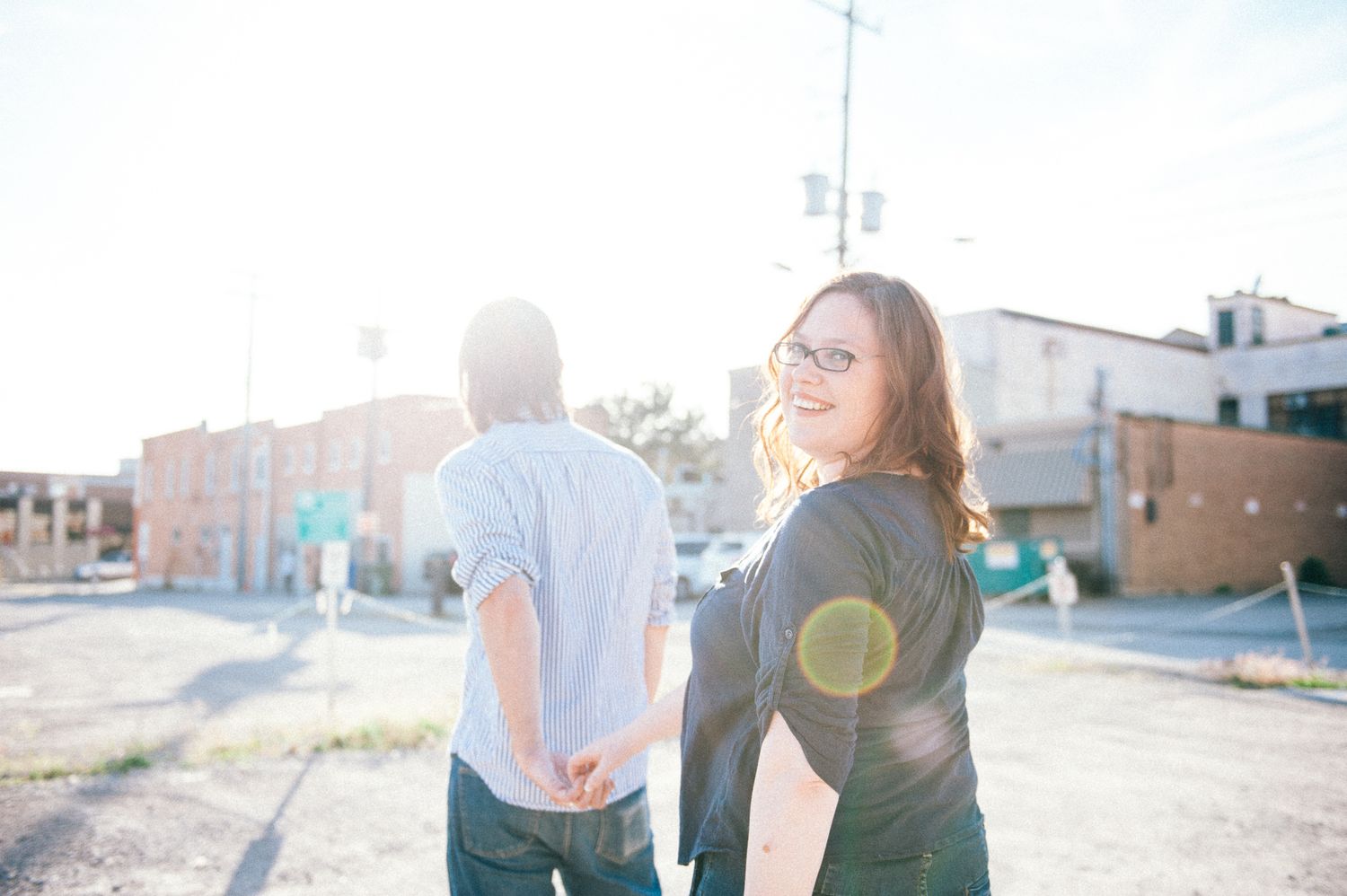Couple holding hands and walking through a city street in golden sunlight.
