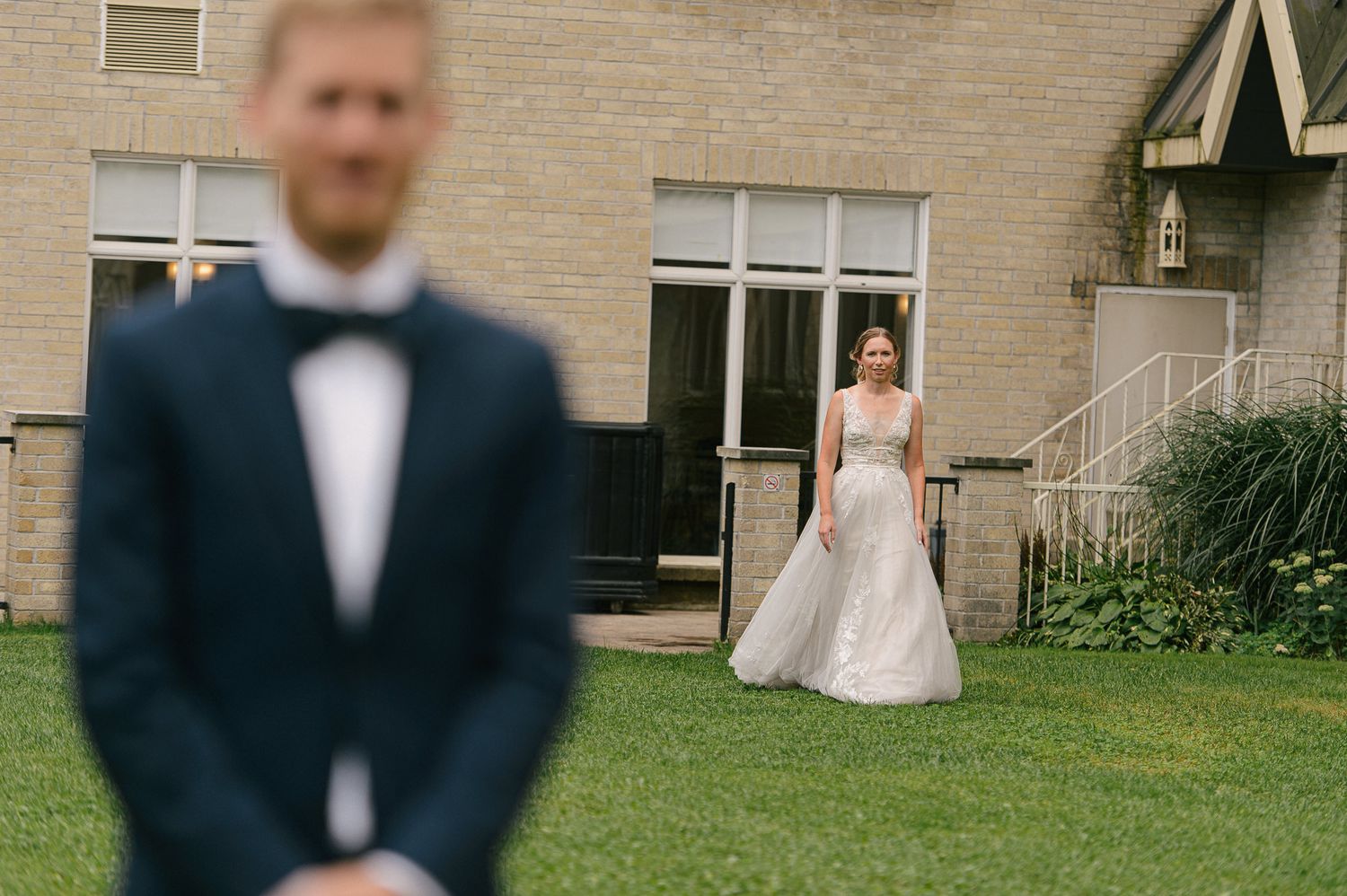 An outdoor wedding scene against a beige brick building with natural landscaping.