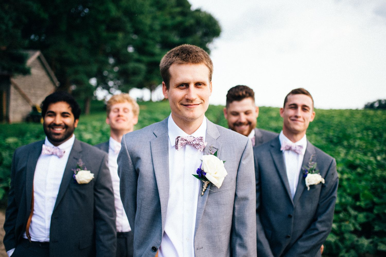 Groomsmen in grey suits standing together outdoors for wedding photo.
