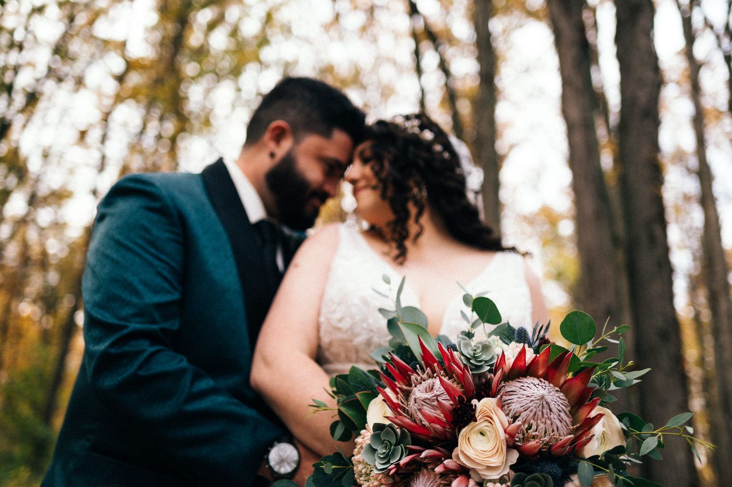 Romantic wedding portrait with burgundy and blush floral bouquet in autumn woodland setting.