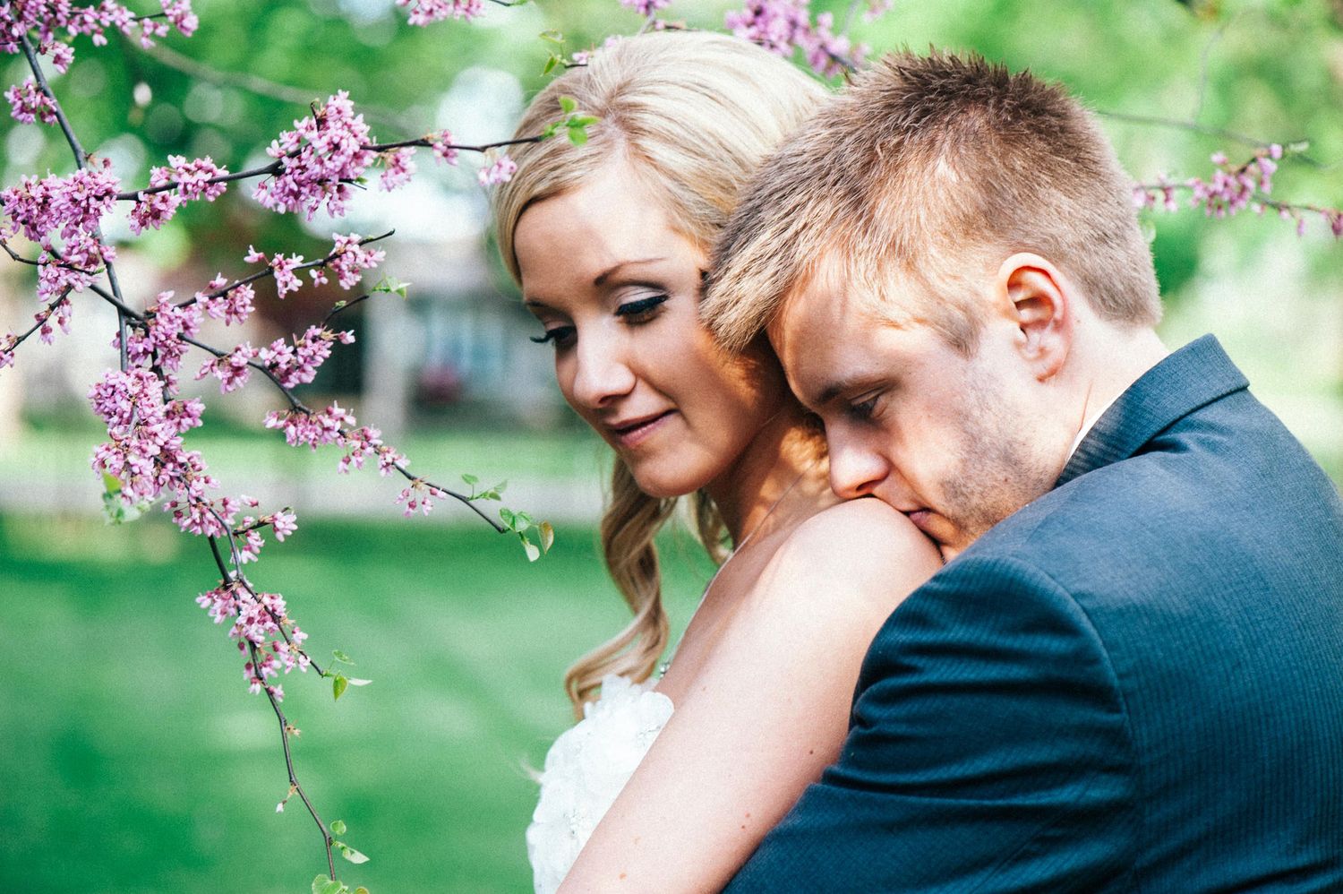 Romantic couple embraces under blooming cherry blossom trees in a garden setting.