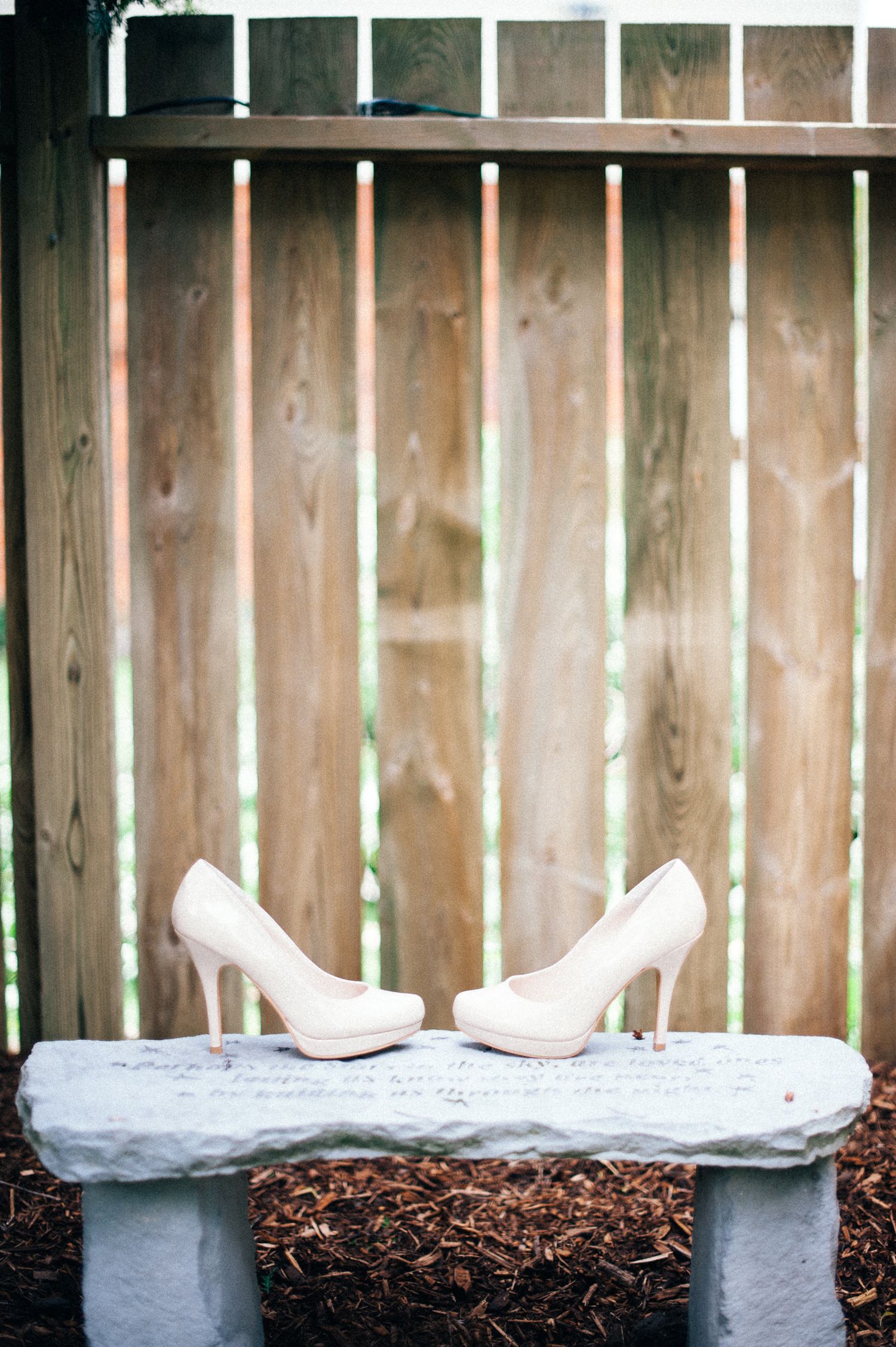 Wedding shoes displayed on white fabric against rustic wooden fence backdrop.