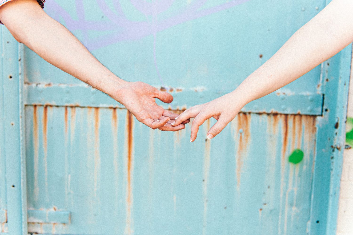 Close-up of two hands reaching toward each other against turquoise background.