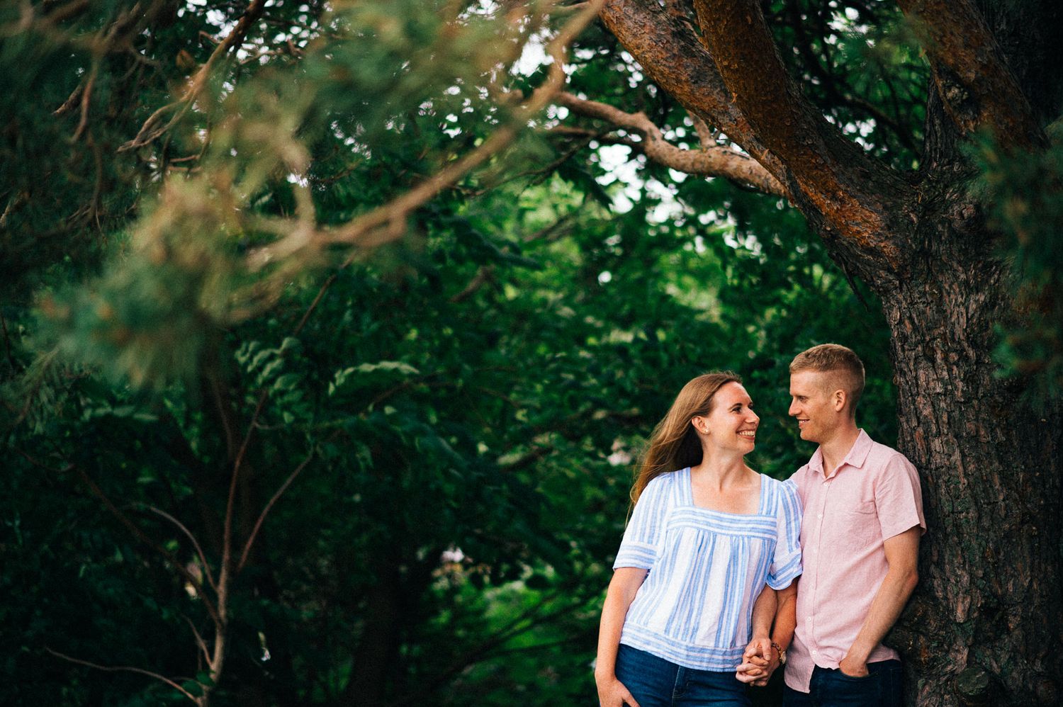 Romantic couple sharing tender moments under a tree in a lush green park.