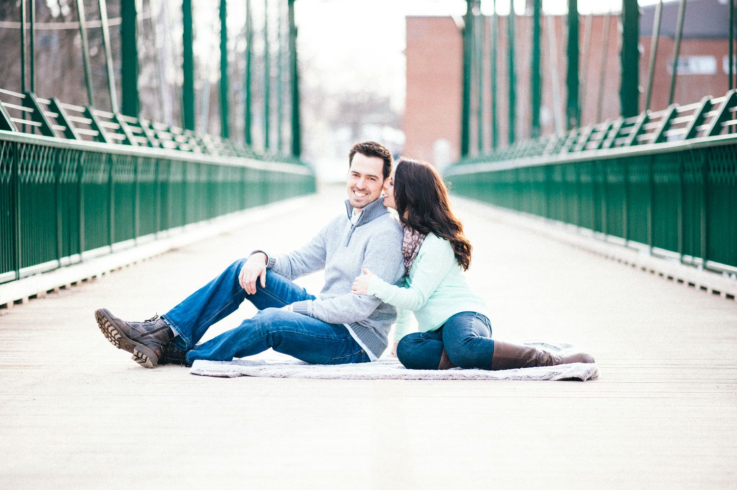 Couple sitting together on urban bridge with industrial backdrop.
