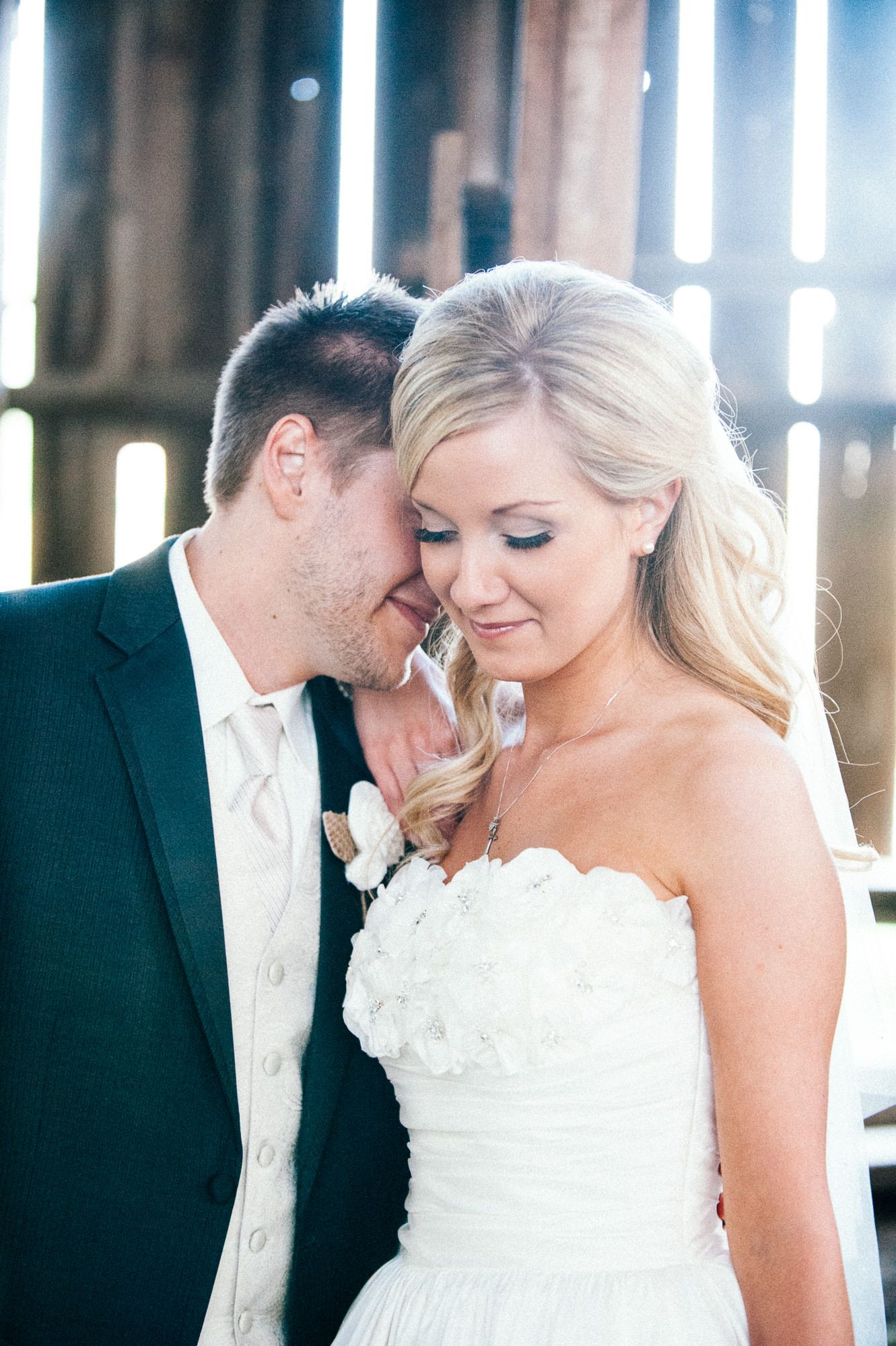 Intimate wedding couple portraits captured in a sunlit barn with dramatic lighting.